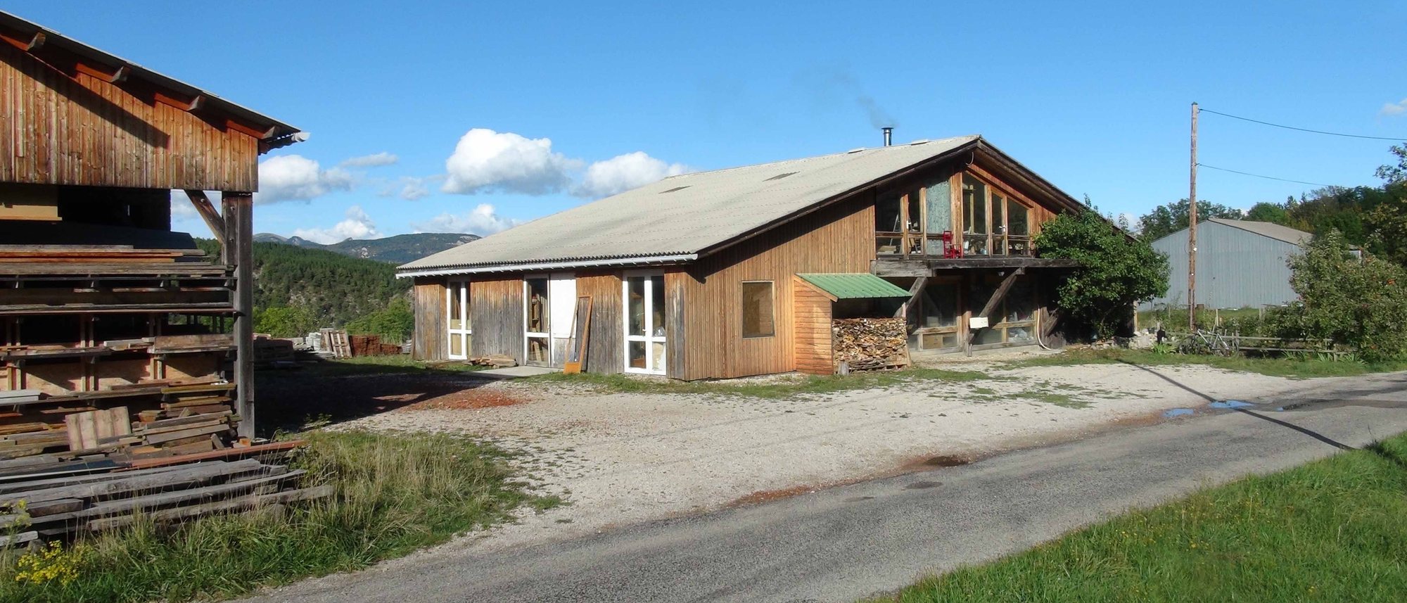 L'atelier de Rossas, hangar en bois et piles de planches sous séchage, montagnes du Diois au fond
