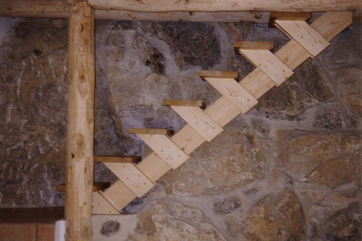 Escalier en bois clair à limon crémaillère posé contre un mur en pierre