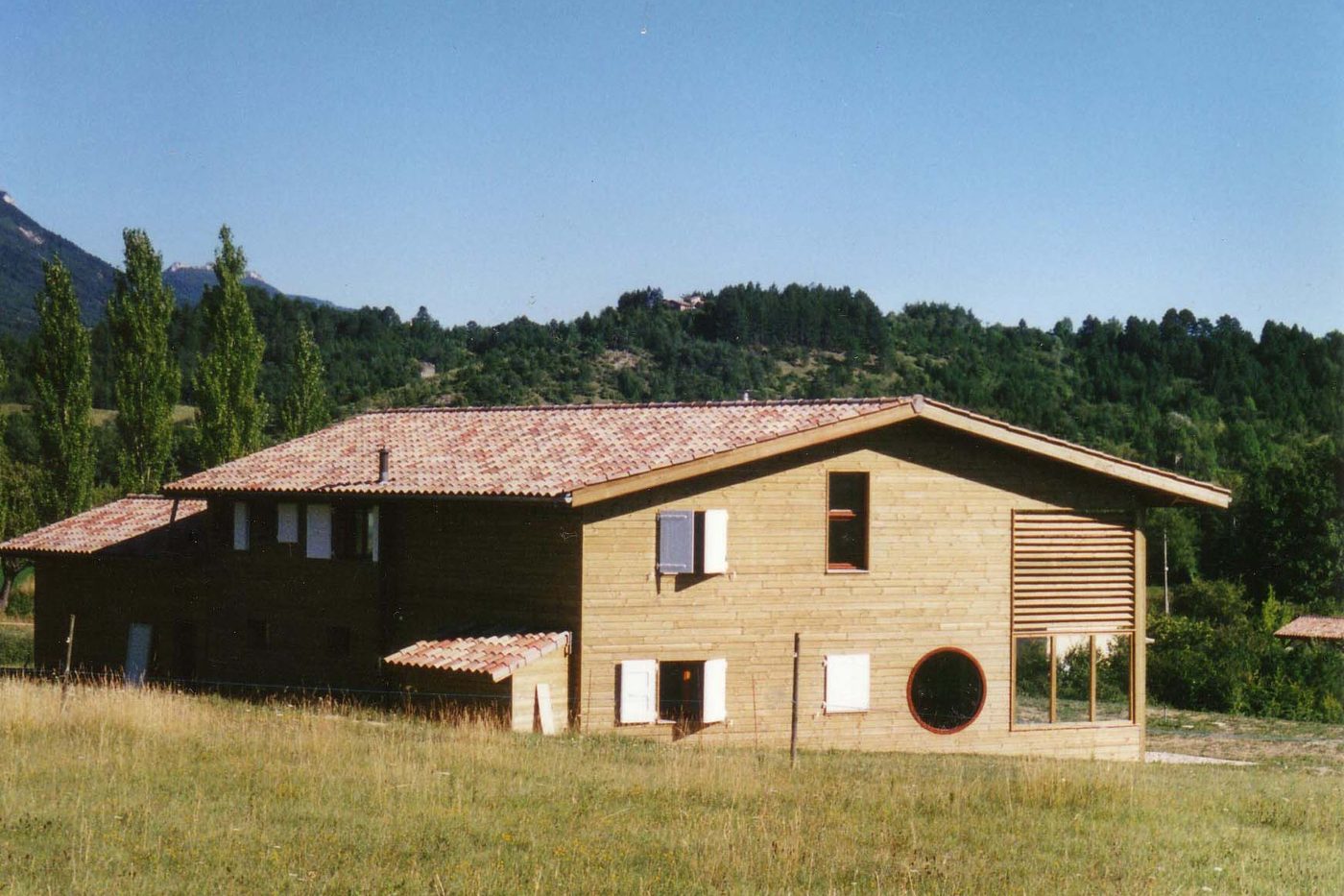 Maison individuelle à ossature bois avec bardage clair, dans un pré face aux montagnes