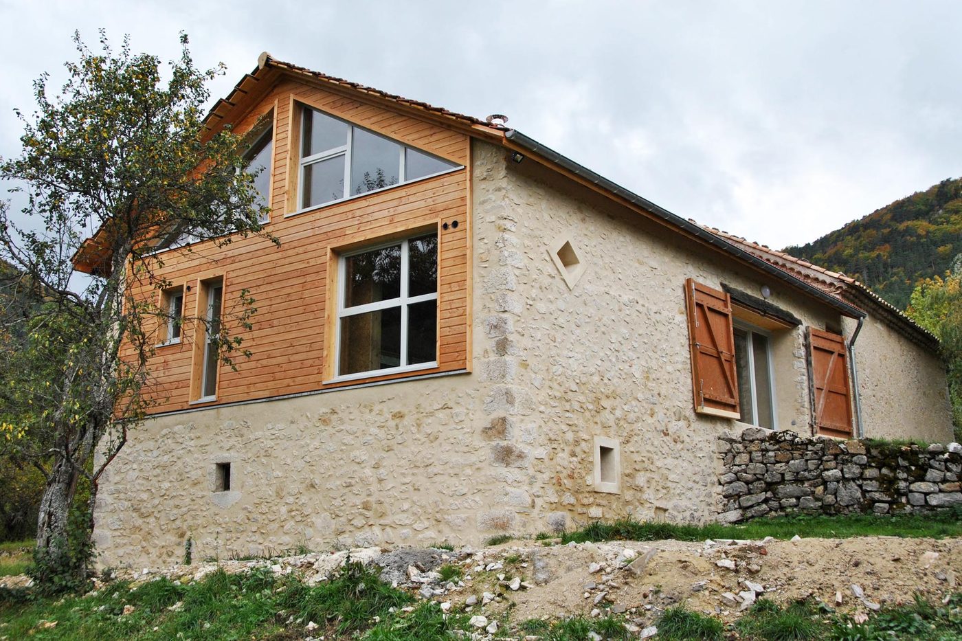 Pignon d'une maison de pierre rénovée, partie haute habillée d'un bardage bois neuf